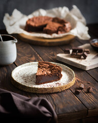 Chocolate cake on a wooden table. A piece of brownie on a brown background. Cocoa and chocolate pieces. Serving dessert.