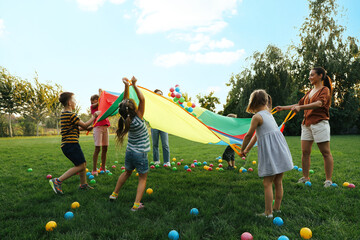 Group of children and teacher playing with rainbow playground parachute on green grass. Summer camp activity - Powered by Adobe