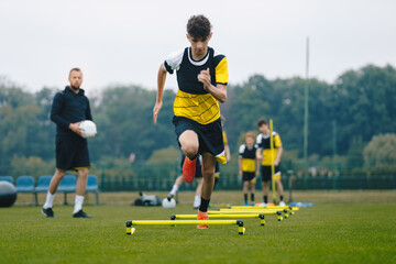 Junior soccer player running fast and ladder skipping. Boys practice football witch young coach. Teenagers on soccer training camp. Youth athletes improving soccer skills on outdoor training