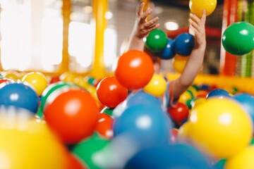 Happy child playing at balls pool playground. Kid playing with multi coloured plastic balls in big...