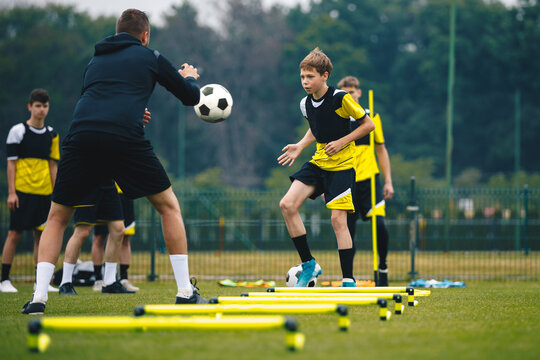 Teenagers on soccer training camp. Boys practice football with young coaches. Junior level athletes improving soccer skills on outdoor training. Player kick soccer ball to coach and ladder skipping