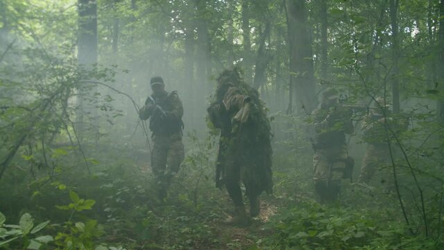 Military squad of armed soldiers in combat gear wading through forest area in dense fog, getting ambushed with explosions of enemy fragmentation grenades, spreading out to avoid casualties