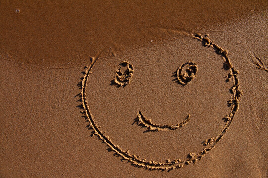 emoticon face painted on jetted beach sand by sea