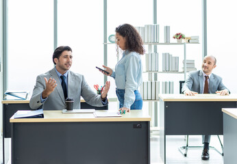 Businessman and businesswoman sharing laptop smartphone while sitting at a desk in office building room.