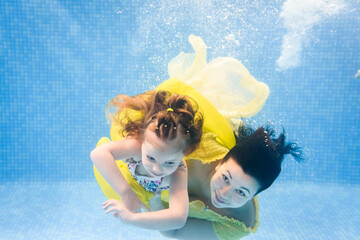 Mother holds daughter, submerged under water, swimming under water in paddling pool. Diving baby....