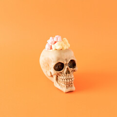Halloween  skull with candies on orange background. Minimal scary halloween concept.