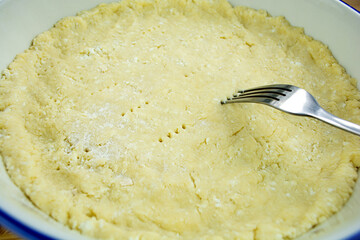 Person piercing with a fork the raw dough that is going to fill with the ingredients tart or a quiche. Cooking at home.