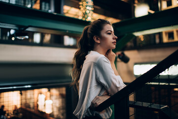 Contemplative Caucasian woman in white shirt thoughtful looking away and thinking about weekend leisure spending in public place, pensive hipster girl with brunette hair feeling pondering indoors