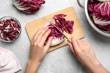 Woman cutting fresh ripe radicchio at light grey marble table, top view