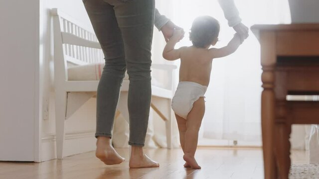 baby learning to walk toddler taking first steps with mother helping infant teaching child at home 