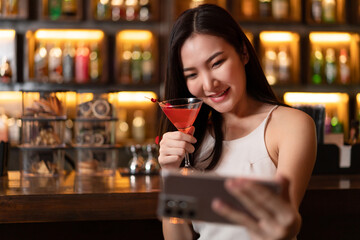 Nightlife concept a sexy girl with smiling face doing selfie on her smartphone while hold a vivid pink champaign in the night bar