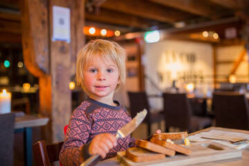 Fototapeta na wymiar Preschool child, cute boy, eating bread in a restaurant, cozy atmosphere, local small restaurant in Tromso