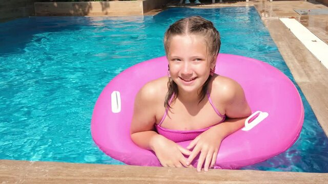 Happy beautiful girl relaxing in swimming pool with turquoise water. Girl floating on pink inflatable ring. Traveling and vacation concept