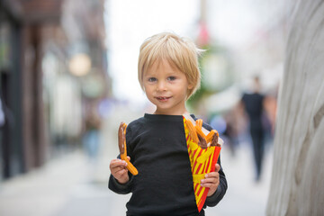 Cute blond child with black shirt, eating churros on the street in the city of Stockhlom, sweet desert sold on every corner