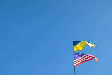 Ukrainian and American flag on a blue sky background. Friendship of peoples and diplomatic mission. Yellow-blue and stars-striped fabric on a flagpole.