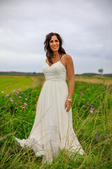Fototapeta na wymiar Glückliche junge Braut im Hochzeitskleid im Blumenfeld