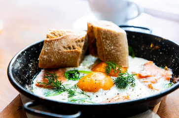 Two delicious Fried eggs cooked in a vintage pan with smoked salmon and spinach, served with two pieces of bread for an healthy breakfast