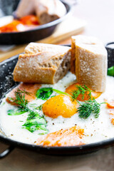 Two delicious Fried eggs cooked in a vintage pan with smoked salmon and spinach, served with two pieces of bread for an healthy breakfast