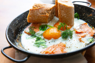 Two delicious Fried eggs cooked in a vintage pan with smoked salmon and spinach, served with two pieces of bread for an healthy breakfast