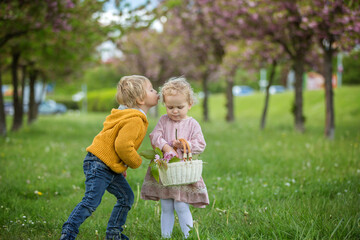 Beautiful children, toddler boy and girl, playing together in cherry blossom garden,boy giving a little bouquet of wild flowers to the girl. Kids friendship