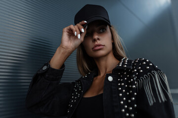 Beautiful cool young woman with a black cap in a black fashionable denim jacket with rhinestones...