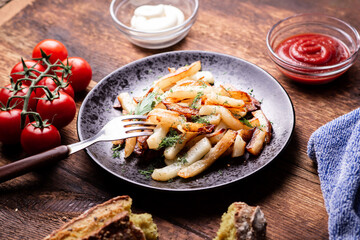 Delicious fried chopped potatoes with ketchup, mayonnaise and herbs on a wooden background.