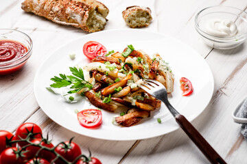 Fried potatoes in a white plate with green onions, parsley, tomatoes on a white wooden background.