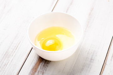 Raw egg in a plate on a white wooden background.