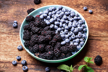 blueberries and blackberries on a plate on a dark wooden background. Fruit, berry background.