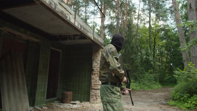 Counter-terrorist group of soldiers hiding around corner outdoors, applying chokehold to terrorist in camouflage and balaclava helmet with automatic gun on patrol near abandoned building in forest