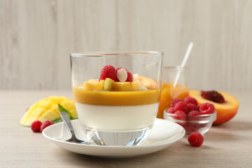 Delicious panna cotta with mango coulis, fresh fruit pieces and almond flakes on light wooden table