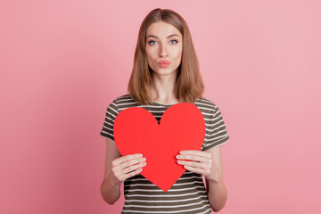 Portrait of nice cute attractive lady holding in hands large paper heart pouted lips send air kiss isolated over pink background