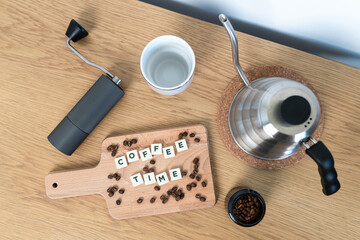 Coffee time - text with a background - Wooden table with kettle, coffee beans, mug and grinder