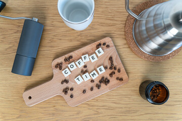 Coffee time - text with a background - Wooden table with kettle, coffee beans, mug and grinder