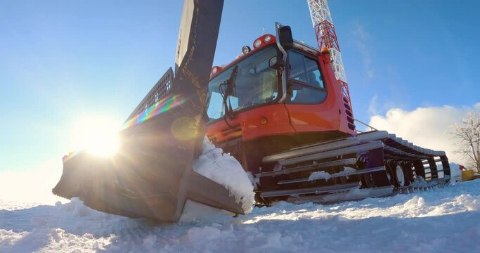 Red modern snowcat ratrack with snowplow grooming the snow and preparing the ski slope piste in a skiing winter resort. Heavy machinery mountain equipment track vehicle