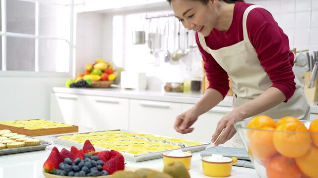 4K Asian woman bakery shop owner preparing bakery in the kitchen. Female baker baking tart dough for making fruit tart on the table. Small business entrepreneur and indoor activity lifestyle concept.