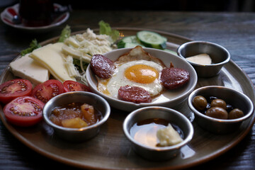 Turkish breakfast ready to eat. There are egg with sausage, sliced tomatoes and cucumbers, honey, jam, olives at the table.