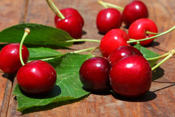 Ripe red sweet cherry with green leaves on the rough wooden background 