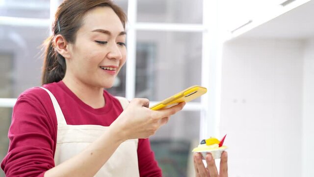 4K Asian woman bakery shop owner using smartphone photography dessert bakery  for advertising on social media in the kitchen. Small business entrepreneur and online marketing food delivery concept