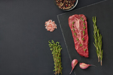 Raw fresh beef top blade steak on stone board, with rosemary and thyme and spices ready for...