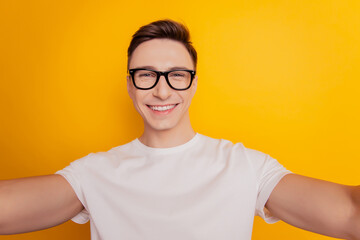 Portrait of handsome positive guy hold camera take selfie beaming smile on yellow background