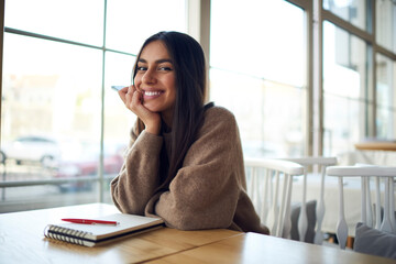 Portrait of cheerful Middle Eastern female student with education notepad posing at table desktop...