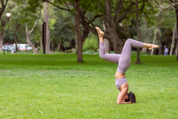 Woman doing yoga asanas in the park on the grass with trees in the background.