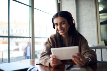 Portrait of cheerful Middle Eastern female blogger using modern touch pad technology and bluetooth...