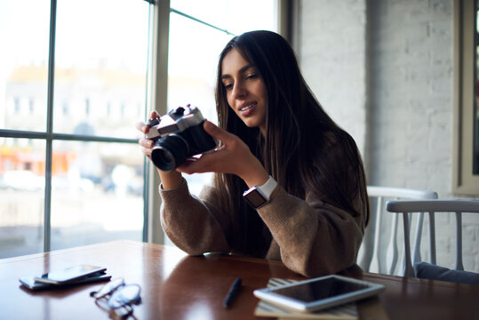 Attractive professional photographer with vintage camera technology editing photo images during leisure time in cafe interior, Middle Eastern hipster girl with retro technology checking pictures