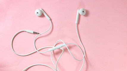 White headphones with wires on a pink background.