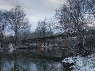 Concrete bridge over river in winter, snow covered riverbanks and trees