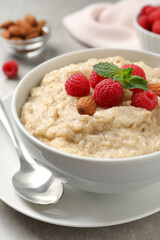 Tasty oatmeal porridge with raspberries and almond nuts served on table, closeup