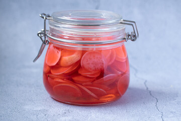 Pickled red radish in glass jar on black background copy space