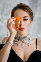 beautiful young woman in a swimsuit sitting on the floor near the window and looking away holds shrimp